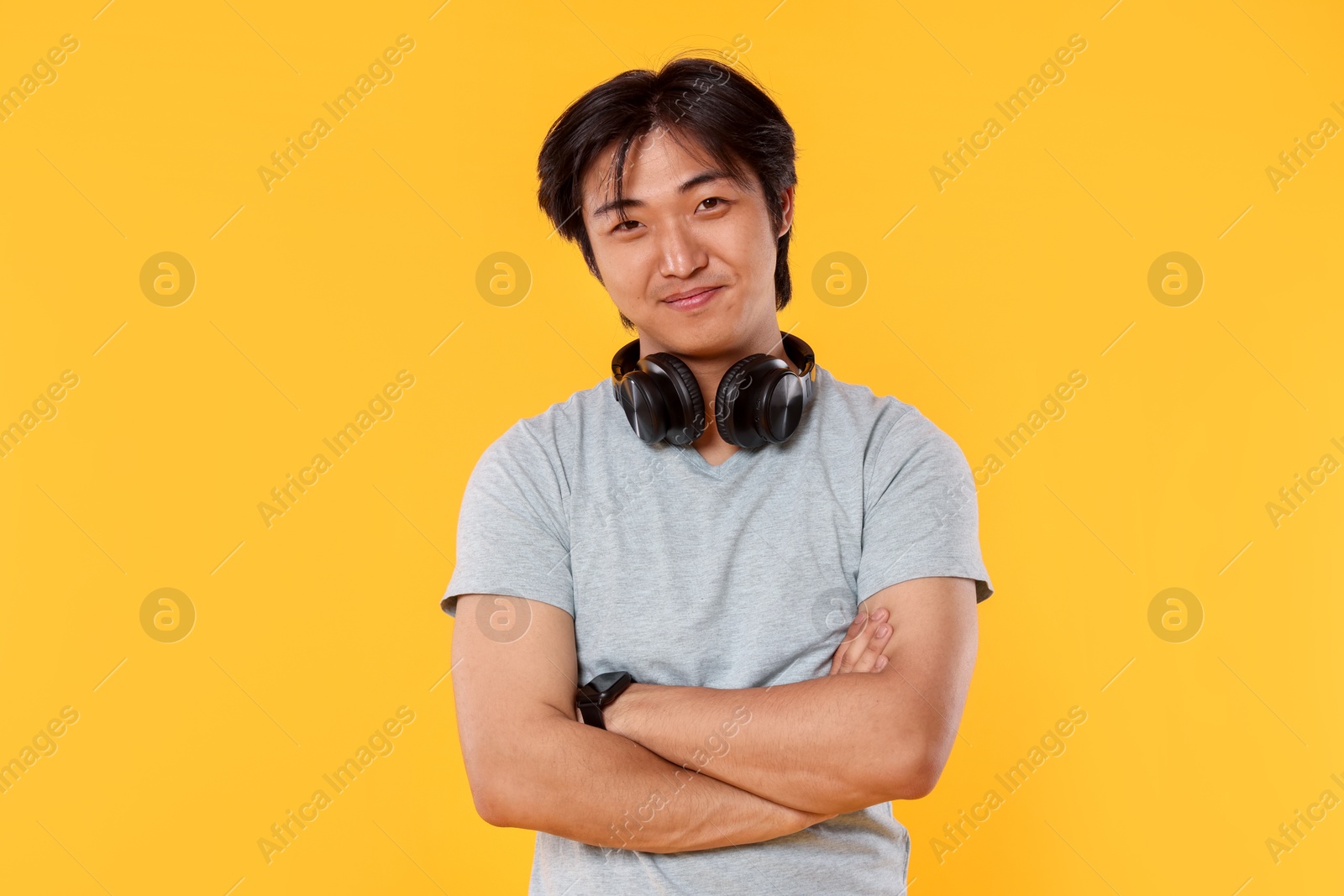 Portrait of handsome Asian man with headphones on yellow background Photo of Portrait of handsome Asian man with headphones on yellow background