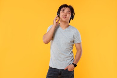 Photo of Portrait of handsome Asian man in headphones on yellow background