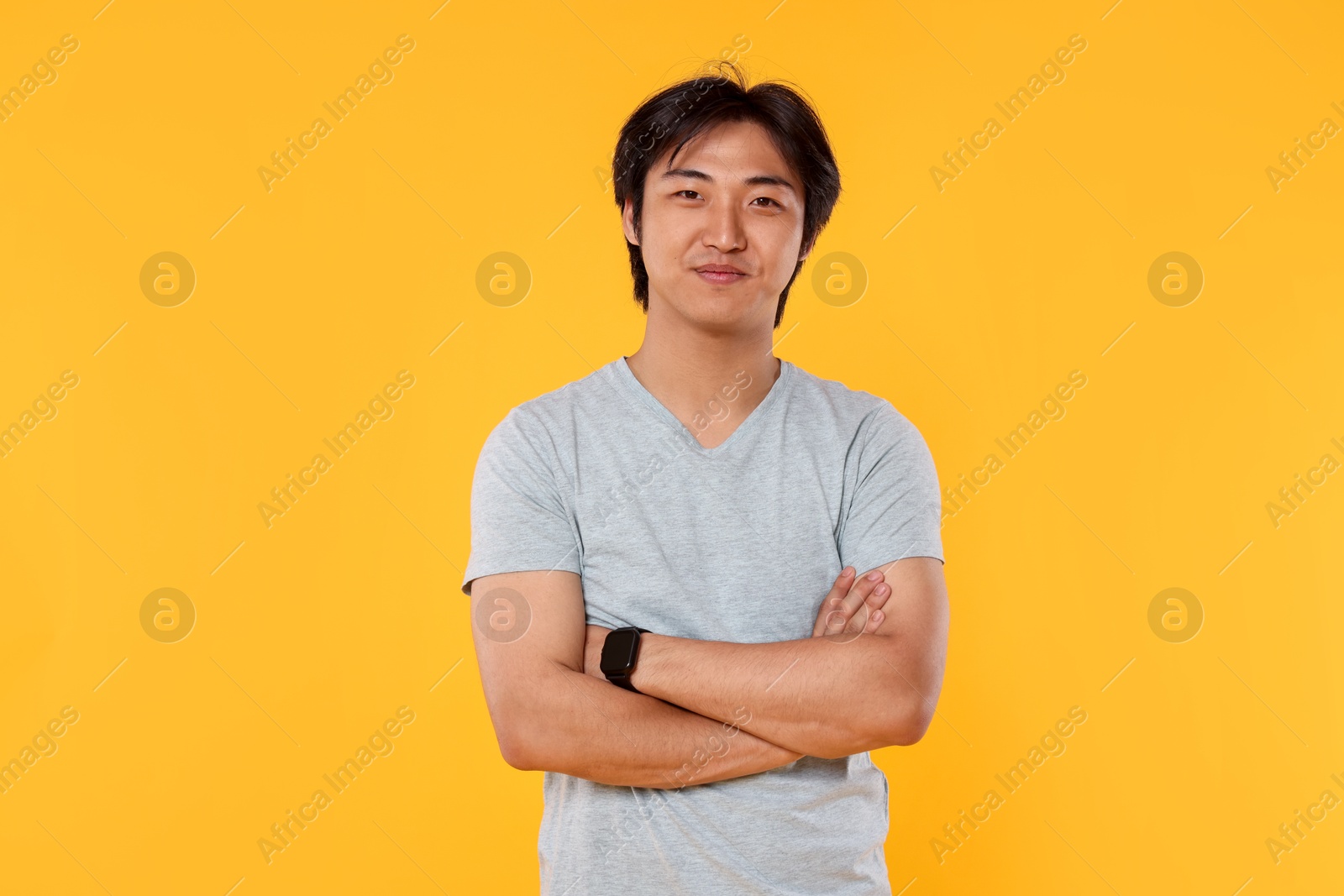 Portrait of handsome Asian man with crossed arms on yellow background Photo of Portrait of handsome Asian man with crossed arms on yellow background