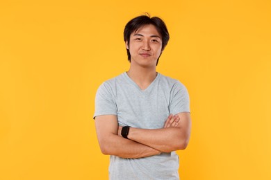 Photo of Portrait of handsome Asian man with crossed arms on yellow background