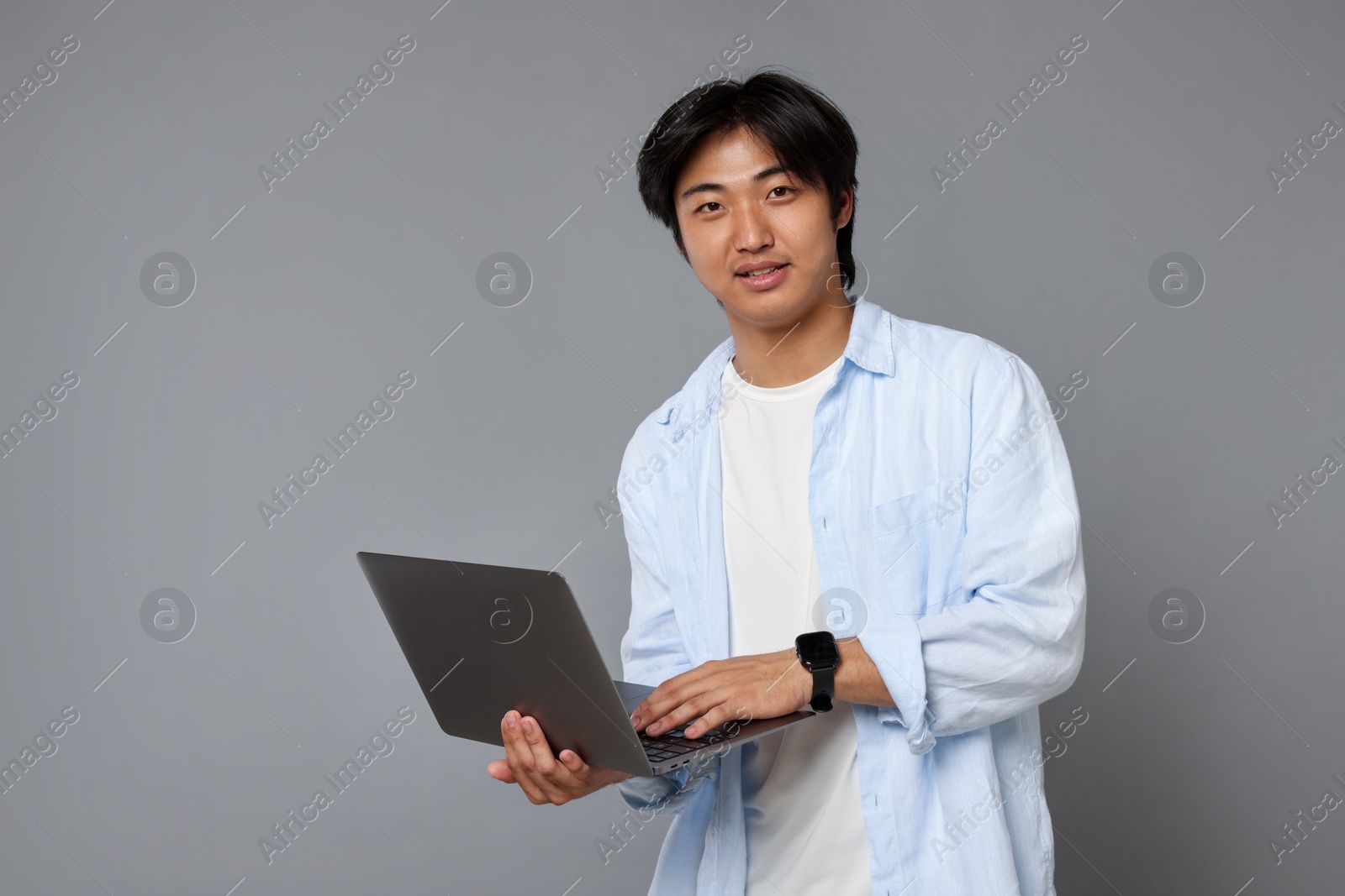 Portrait of handsome Asian man with laptop on grey background Photo of Portrait of handsome Asian man with laptop on grey background