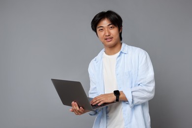 Photo of Portrait of handsome Asian man with laptop on grey background