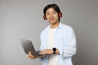 Photo of Handsome Asian man in headphones with laptop on grey background
