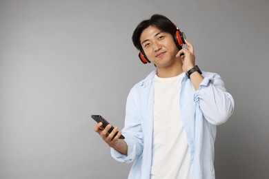Photo of Handsome Asian man in headphones with smartphone on grey background. Space for text