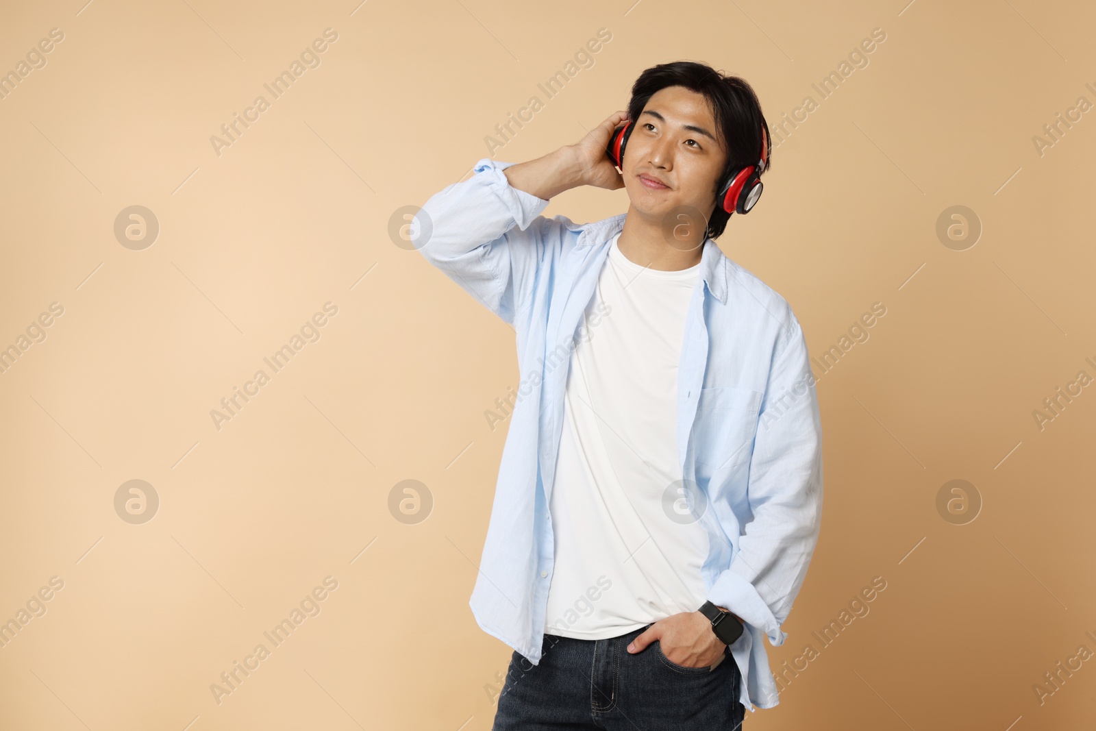 Handsome Asian man in headphones on beige background. Space for text Photo of Handsome Asian man in headphones on beige background. Space for text