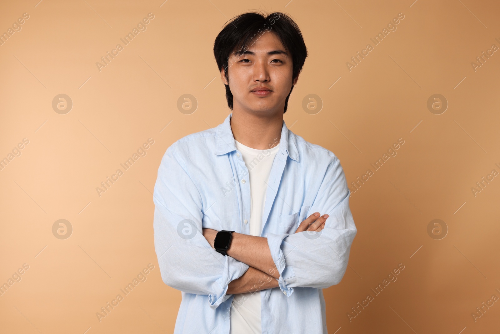 Portrait of handsome Asian man with crossed arms on beige background Photo of Portrait of handsome Asian man with crossed arms on beige background
