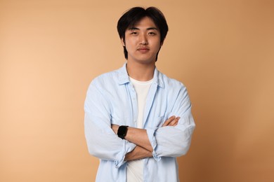 Photo of Portrait of handsome Asian man with crossed arms on beige background