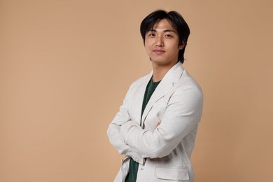 Photo of Portrait of handsome Asian businessman in suit with crossed arms on beige background. Space for text