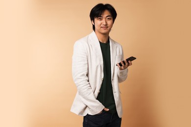 Photo of Portrait of handsome Asian businessman in suit with smartphone on beige background