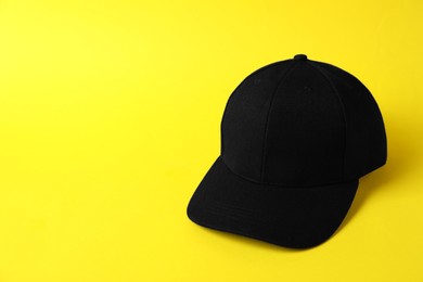 Photo of Black baseball hat on yellow background, space for text