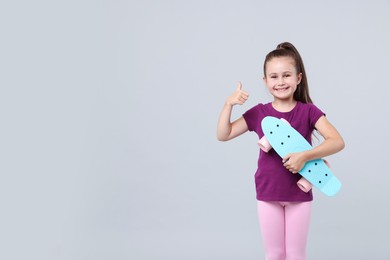 Photo of Little girl with penny board showing thumbs up on light grey background, space for text