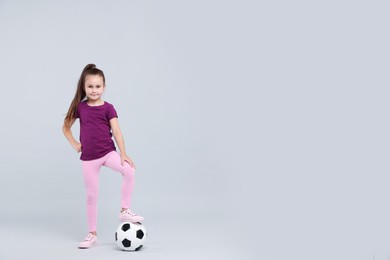 Photo of Little girl with soccer ball on light grey background, space for text