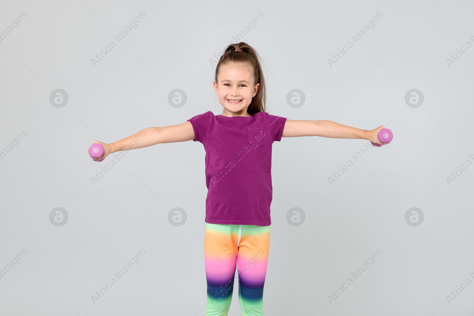 Little girl with dumbbells on light grey background Photo of Little girl with dumbbells on light grey background