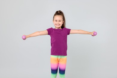 Photo of Little girl with dumbbells on light grey background