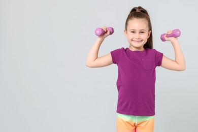 Photo of Little girl with dumbbells on light grey background, space for text