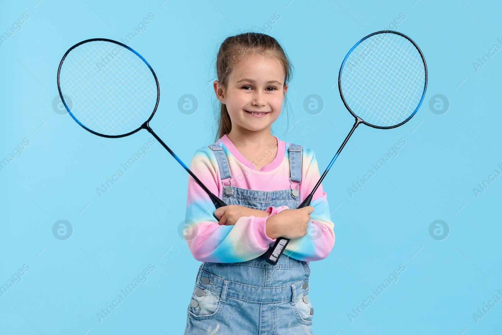 Little girl with tennis rackets on light blue background Photo of Little girl with tennis rackets on light blue background