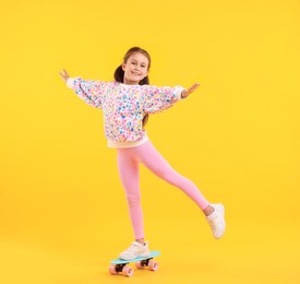 Photo of Little girl with penny board on yellow background, space for text