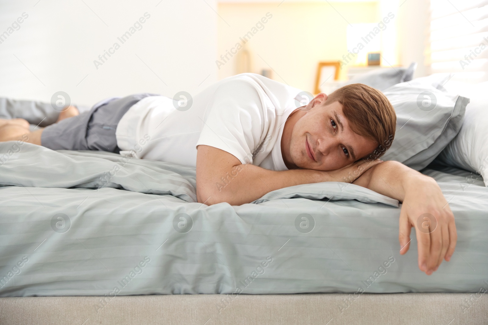 Young man lying on bed with soft mattress at home Photo of Young man lying on bed with soft mattress at home