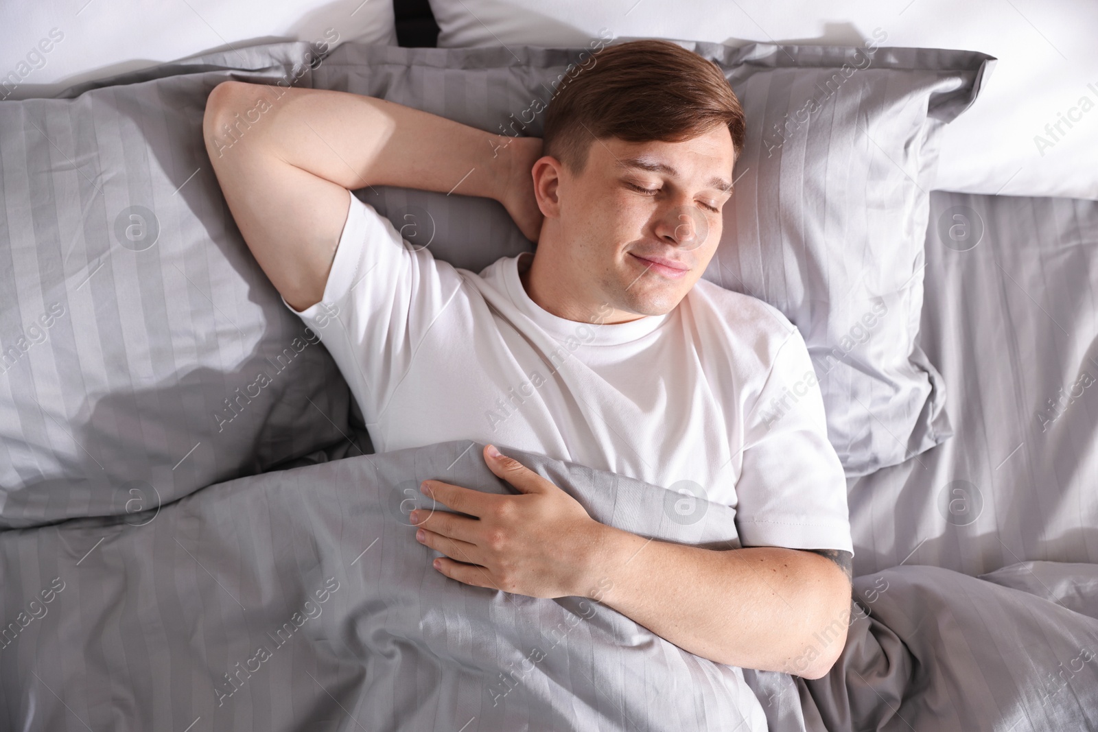 Photo of Young man sleeping on bed with soft mattress at home, top view
