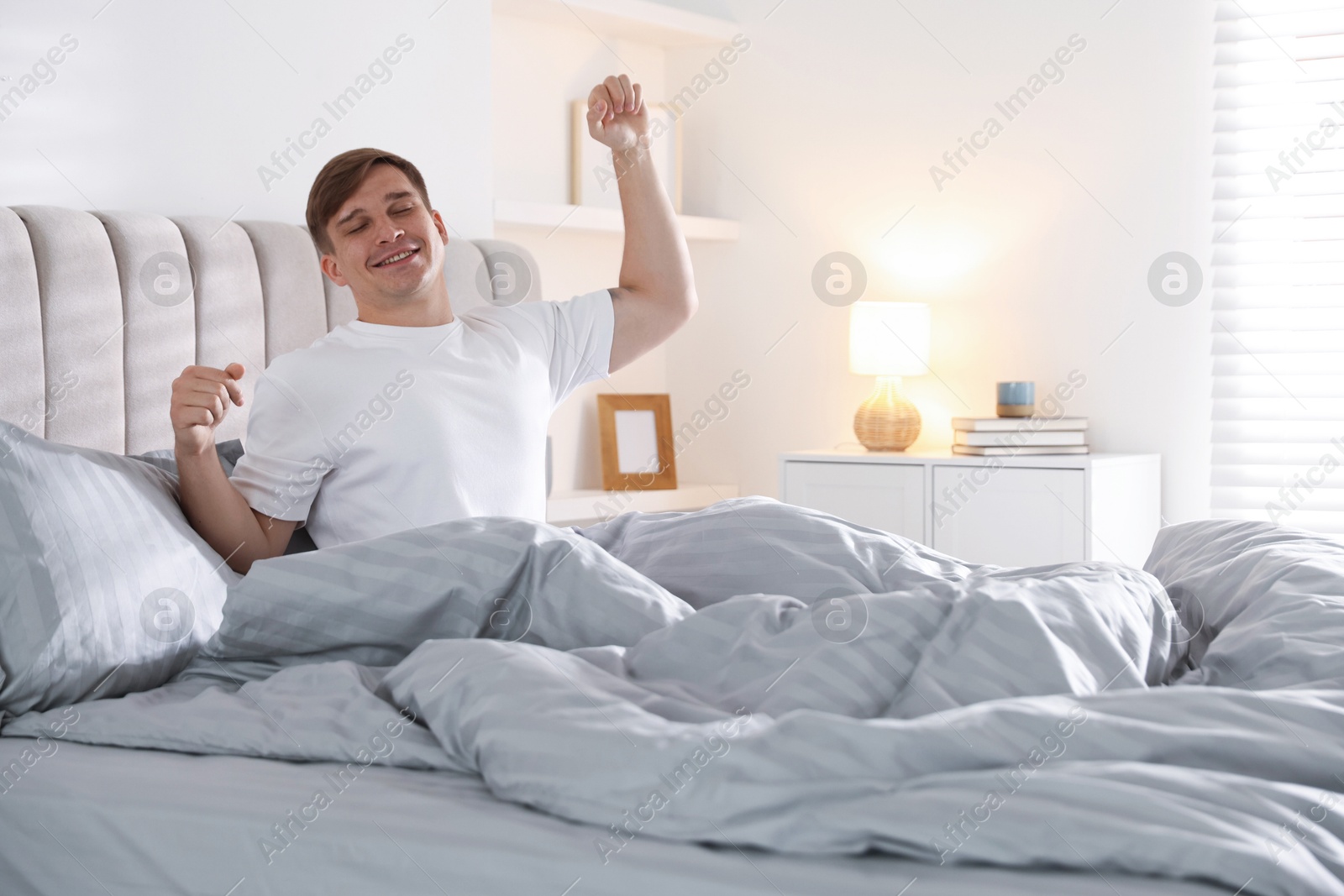 Photo of Young man stretching on bed with soft mattress at home