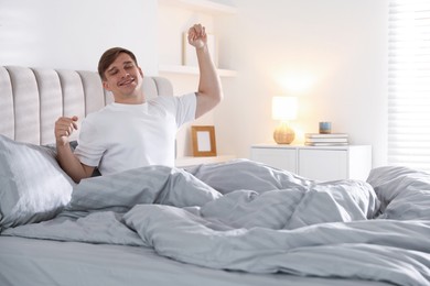 Photo of Young man stretching on bed with soft mattress at home