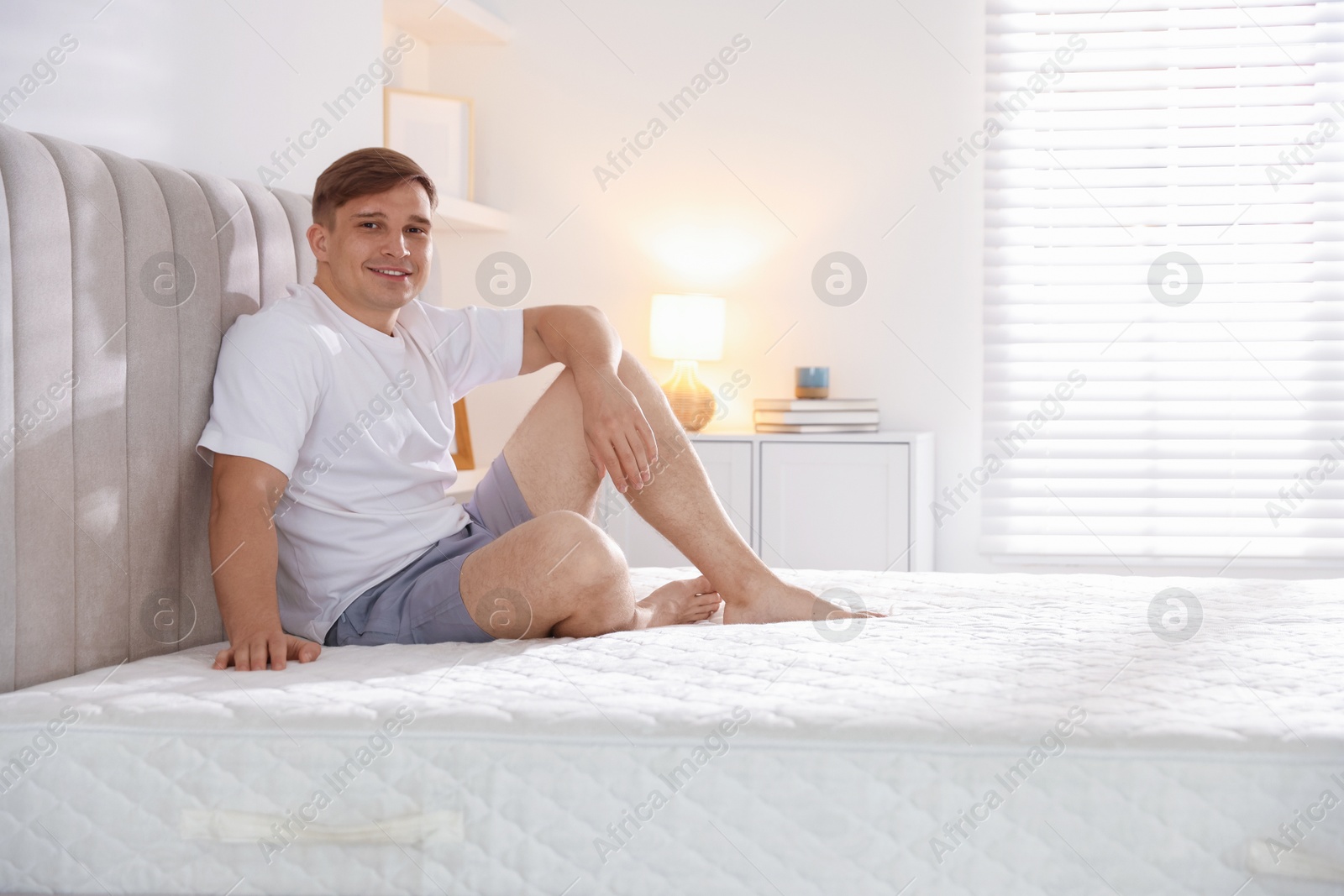 Young man sitting on bed with soft mattress at home, space for text Photo of Young man sitting on bed with soft mattress at home, space for text