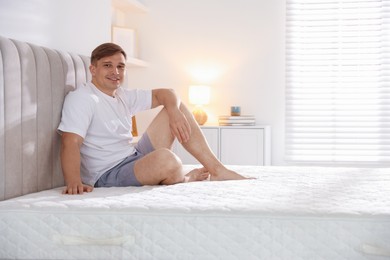 Photo of Young man sitting on bed with soft mattress at home, space for text