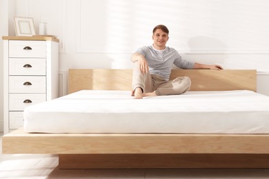 Photo of Young man sitting on bed with soft mattress at home