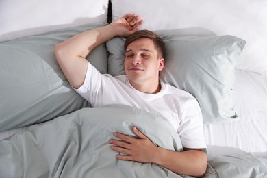 Photo of Young man sleeping on bed with soft mattress at home, top view