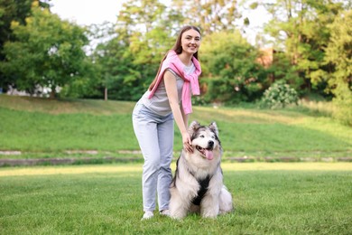 Photo of Smiling woman with her cute Alaskan malamute dog on green grass outdoors