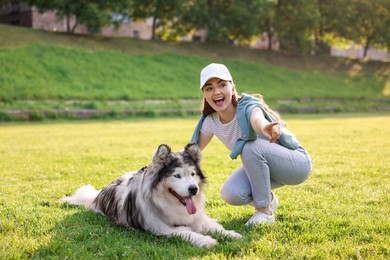 Photo of Happy woman showing something to her cute Alaskan malamute dog on green grass outdoors in morning