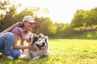 Photo of Smiling woman stroking her cute Alaskan malamute dog on green grass outdoors in morning. Space for text