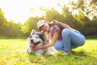Photo of Smiling woman with her cute Alaskan malamute dog on green grass outdoors in morning