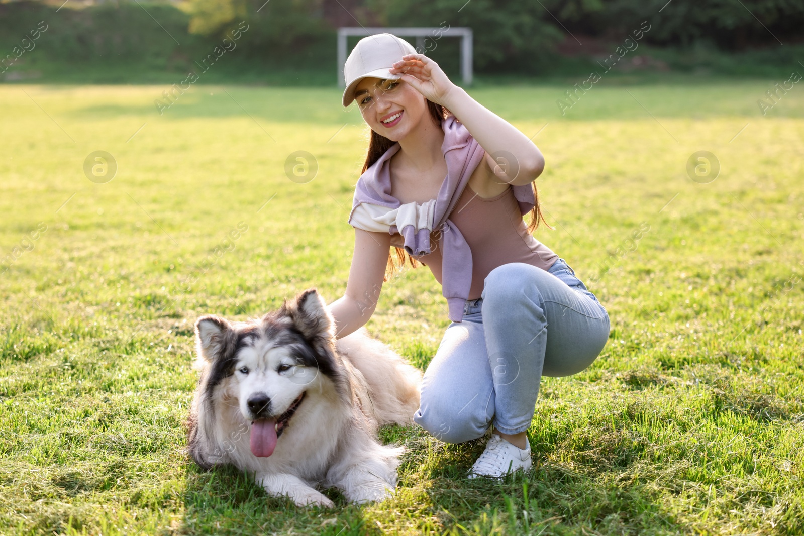 Smiling woman with her cute Alaskan malamute dog on green grass outdoors in morning Photo of Smiling woman with her cute Alaskan malamute dog on green grass outdoors in morning