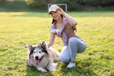 Photo of Smiling woman with her cute Alaskan malamute dog on green grass outdoors in morning