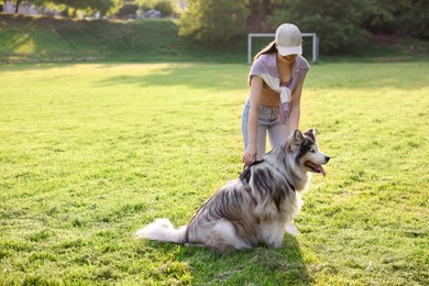 Photo of Smiling woman with her cute Alaskan malamute dog on green grass outdoors in morning. Space for text