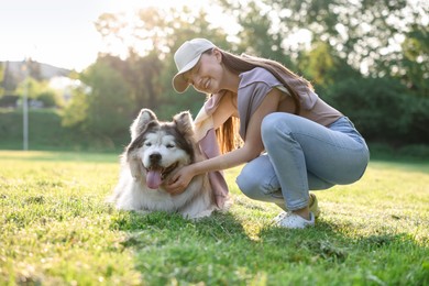 Photo of Smiling woman with her cute Alaskan malamute dog on green grass outdoors in morning