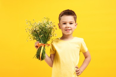 Photo of Smiling little boy with bouquet of beautiful chamomile flowers on yellow background