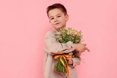 Photo of Portrait of cute little boy with bouquet of beautiful chamomile flowers on pink background