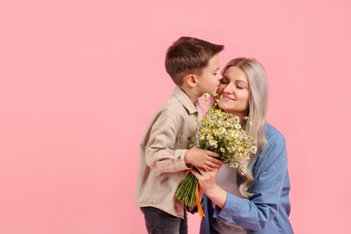 Photo of Little boy kissing his smiling mother with bouquet of beautiful chamomile flowers on white background. Space for text