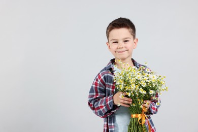 Photo of Portrait of cute little boy with bouquet of beautiful chamomile flowers on light grey background. Space for text