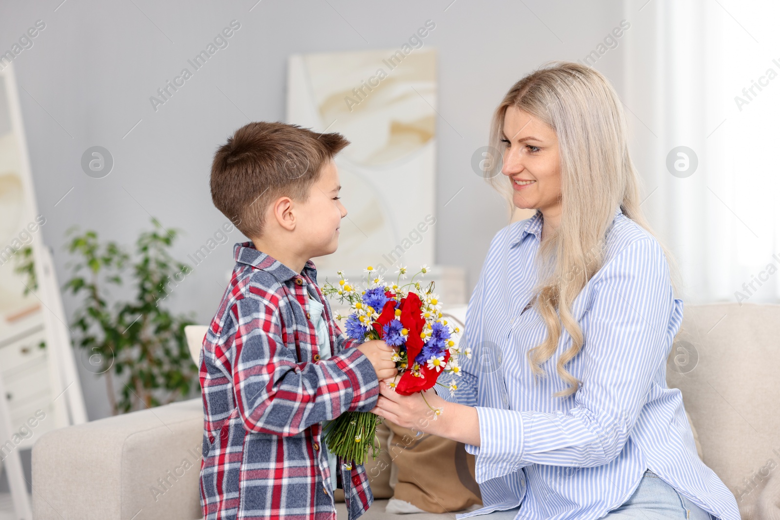 Little boy presenting bouquet of beautiful flowers to his smiling mother on sofa at home Photo of Little boy presenting bouquet of beautiful flowers to his smiling mother on sofa at home