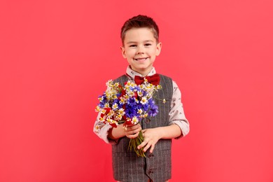 Photo of Portrait of smiling little boy with bouquet of beautiful flowers on red background