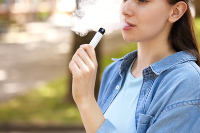 Photo of Young woman using electronic smoking device outdoors, closeup