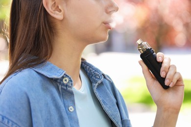 Photo of Young woman using electronic smoking device outdoors, closeup