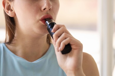 Photo of Young woman using electronic smoking device outdoors, closeup