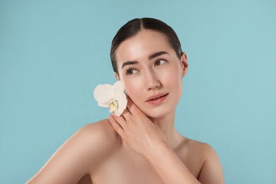 Photo of Beautiful woman with orchid flower after spa treatment on light blue background