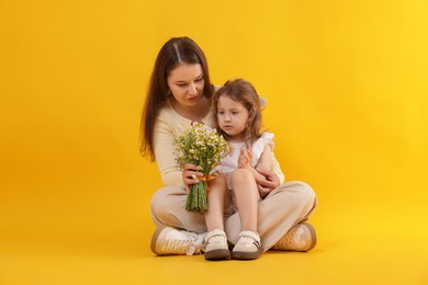 Photo of Mother and her little daughter with bouquet of beautiful chamomile flowers on orange background