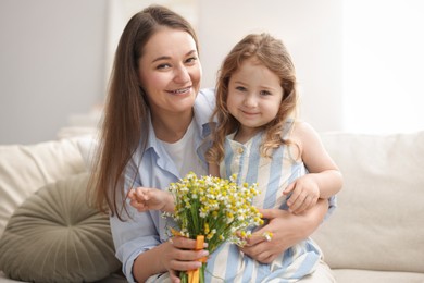 Photo of Mother and her little daughter with bouquet of beautiful chamomile flowers on sofa indoors