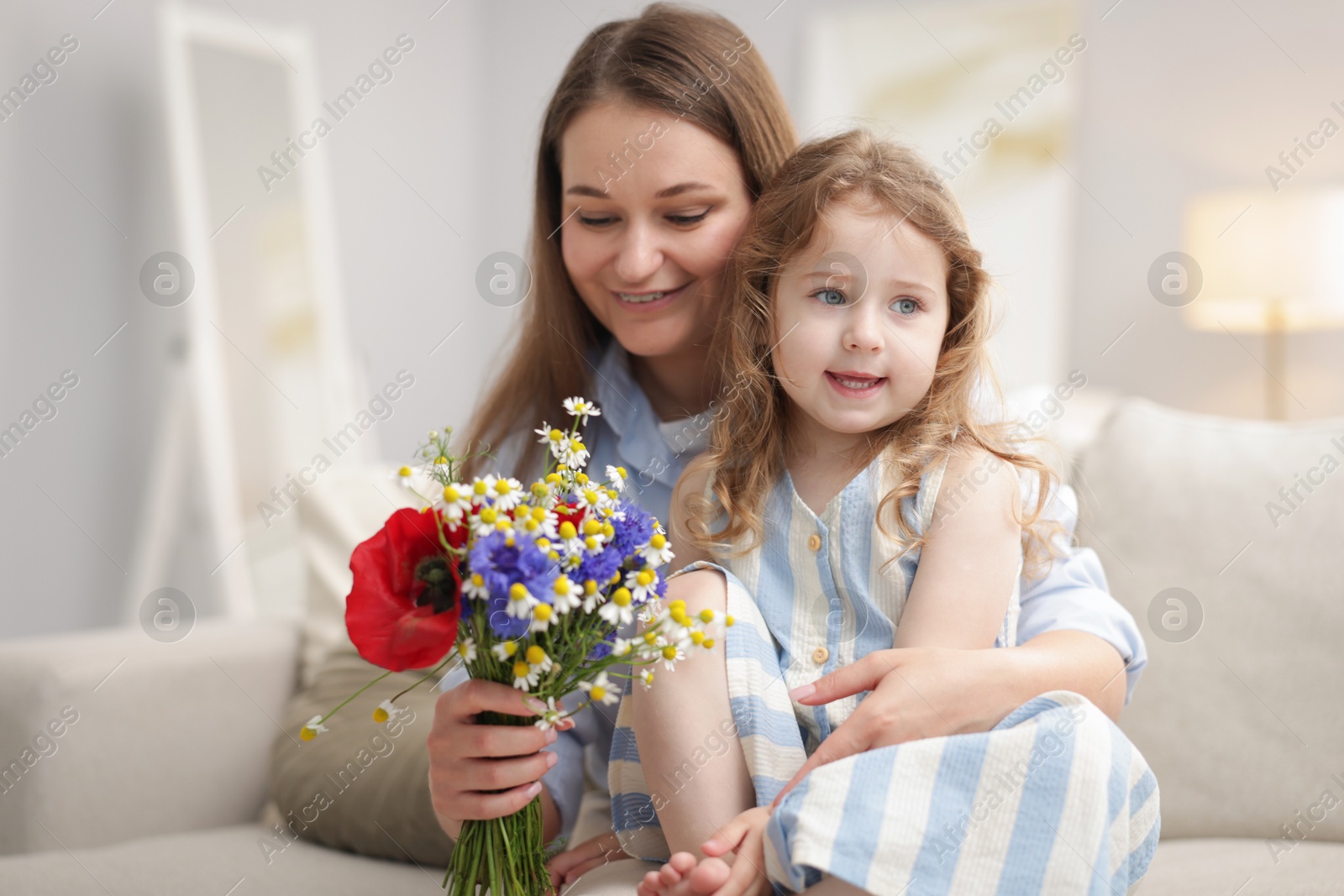 Mother and her little daughter with bouquet of beautiful flowers on sofa indoors Photo of Mother and her little daughter with bouquet of beautiful flowers on sofa indoors